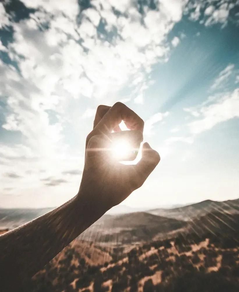 Die Sonne scheint durch die Spalten der Finger einer Hand hindurch.